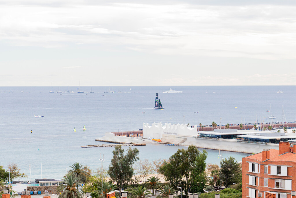 Vista del mar y del puerto de Barcelona con un barco de la Copa América navegando, desde la terraza del encuentro de NTT DATA
