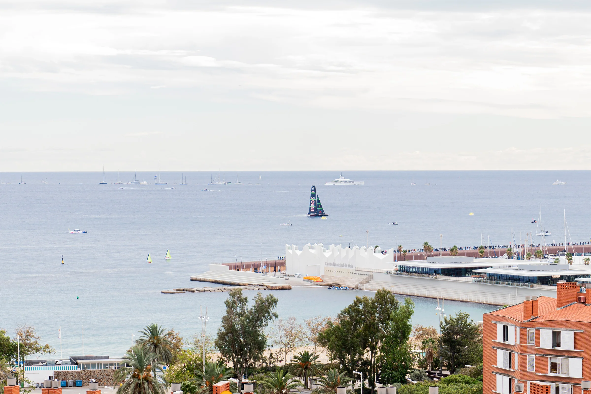 Un barco de la Copa América navegando frente al puerto de Barcelona, visto desde la terraza del encuentro de NTT DATA