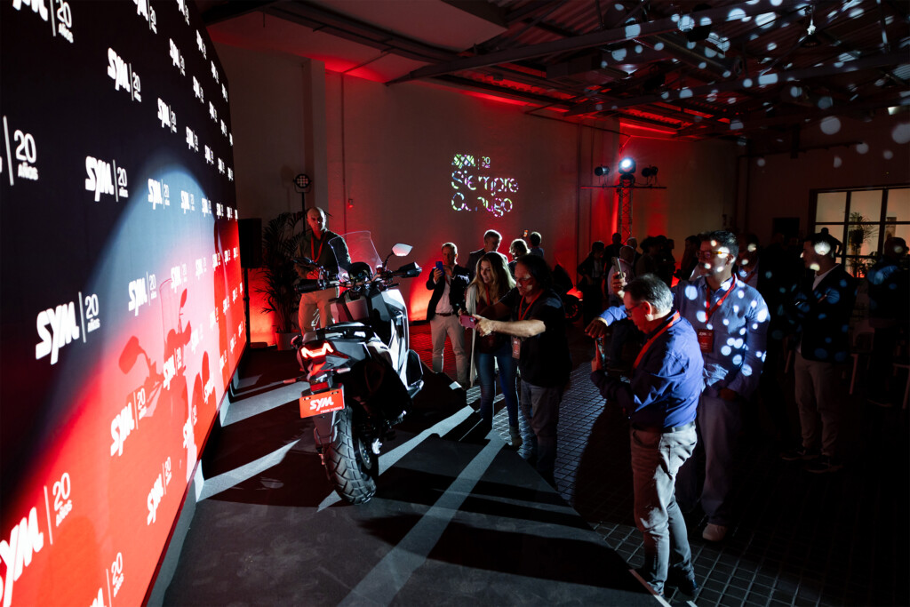 Guests around a SYM scooter beside the branded wall with the SYM España 20 years logo