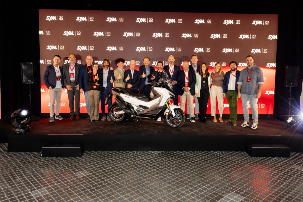 Team photo on stage at SYM España’s 20th anniversary, in front of the backdrop with the SYM 20 years logo