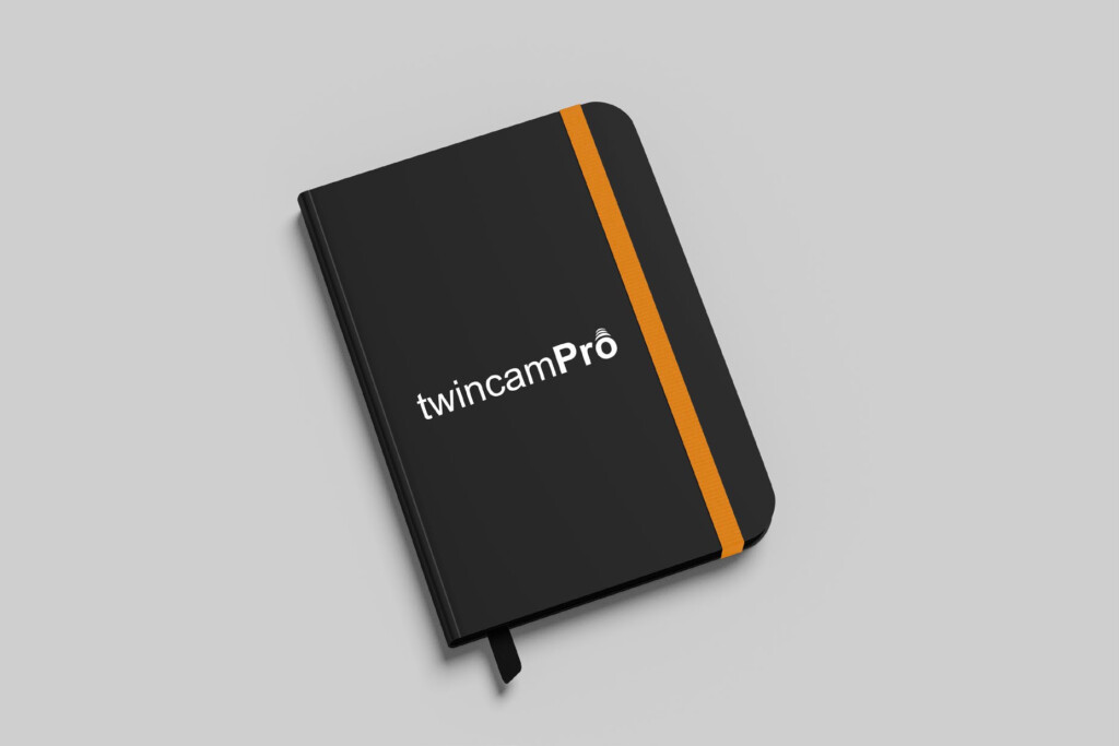 Libreta negra de TwincamPro con el logotipo en blanco y goma naranja